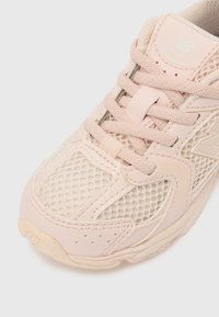 hele roosa sportlik toss, mis on valmistatud võrgust ja sünteetilistest materjalidest, varustatud paeltega sulgemisega, polsterdatud keele ja külje logodetailiga.