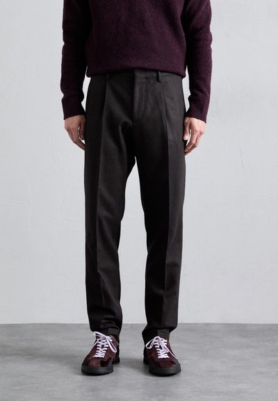 Pantalons sombres, ajustés, avec des jambes droites et une finition nette, associés à des baskets en suède bordeaux avec des lacets blancs et un design texturé.