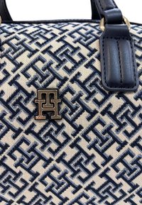 Borsa in tela con motivo geometrico blu navy su sfondo crema. Presenta accenti in pelle e una placca con logo metallico. Forma strutturata.