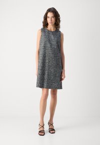 Zwart-wit gevlekte mouwloze jurk met een ontspannen pasvorm, medium lengte en ronde halslijn; gecombineerd met zwarte sleehak sandalen.