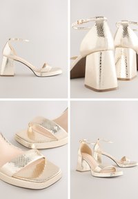 Arany fémes magassarkú szandálok texturált felülettel, négyzet alakú orral, bokapánttal és blokk sarokkal a stabilitás érdekében.