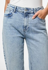 Svijetloplave traperice s visokim strukom, koje imaju klasičan dizajn s pet džepova i vidljive detalje šivanja.