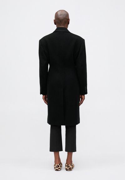 Zwart wollen blend overjas met een op maat gemaakte uitstraling, lange silhouet en gelapt kraag. Draag het over een paar grijze broeken en een paar schoenen met luipaardprint.