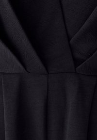 Črn teksturiran material z globokim V-izrezom in nabranim dizajnom, ki prikazuje droben rebrast vzorec in gladke gube.