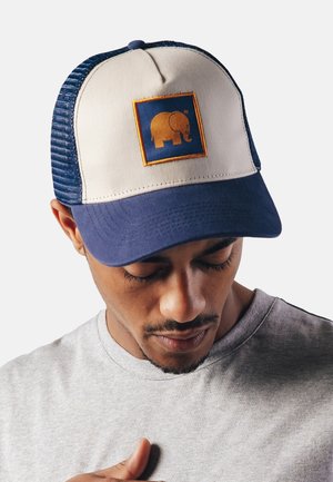 Truckermütze mit einem sandfarbenen Vorderteil, einem marineblauen Schirm und Netzseiten. Verfügt über ein quadratisches Patch mit einem orangefarbenen Elefantenmotiv. Verstärkte Nähte überall.