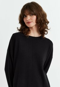 Maglione nero in maglia con vestibilità ampia, scollatura rotonda e spalle cadenti. Presenta un sottile dettaglio di cucitura sul davanti. Texture morbida.