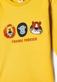 Gul bomulds sweatshirt med tre dyreansigt: en løve, en abe og en tiger, med teksten "VENNER FOR EVIGT" nedenfor i orange broderi.