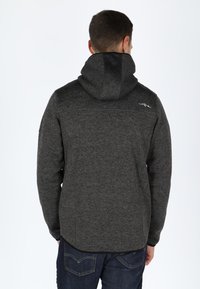 Grijze fleece hoodie met een gestructureerde afwerking, voorzien van een hoge kraag en verstelbare capuchon, gecombineerd met donkere jeans. Eenvoudig ontwerp, geen zichtbare logo's.