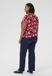 Blusa a fiori rossi con maniche corte, abbinata a jeans in denim blu scuro e scarpe flat nere. Tessuto morbido al tatto, vestibilità casual.