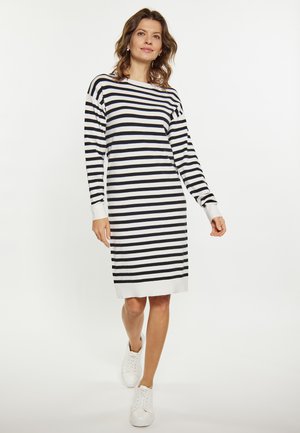 Gestreiftes Strickkleid in Schwarz, Weiß und Marineblau. Lange Ärmel, lockere Passform, Stricktextur und gerippte Bündchen. Kombiniert mit weißen Sneakers.
