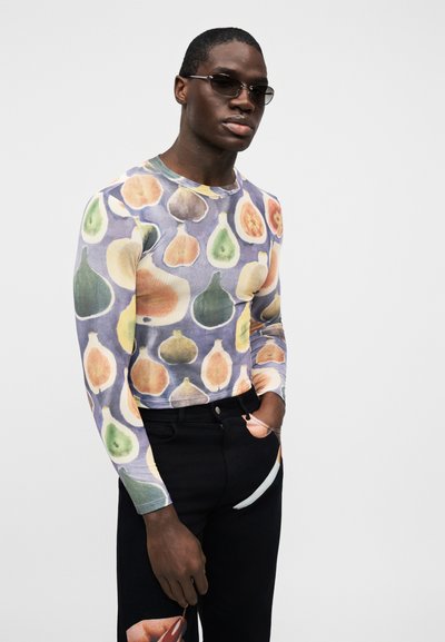 Košeľa s dlhým rukávom zdobená farebným ovocným vzorom na svetlofialovom pozadí. Čierne nohavice s vreckovým detailom dopĺňajú vzhľad.