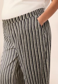 I pantaloni a righe presentano righe verticali bianche e nere, una cintura elastica e tasche laterali, realizzati in un tessuto leggero e traspirante.
