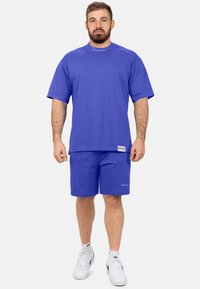 Completo sportivo blu composto da una maglietta aderente e pantaloni corti, realizzati in un tessuto liscio, con dettagli del logo e accenti a contrasto.