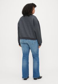 Mörkgrå oversized sweatshirts med sänkta axlar, kombinerat med ljusblå utsvängda jeans, bärs med svarta skor. Bakifrån, enkel bakgrund.
