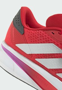 Red athletic shoe with mesh upper, white stripes, and a grey heel accent. Features a cushioned sole with a purple gradient detail.