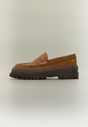 Mocassino in pelle scamosciata marrone con suola spessa nera scolpita e dettagli cuciti, mostrato di profilo su sfondo neutro.