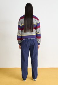Multifarvet stribet sweatshirt i grå, lilla og rød med en afslappet pasform, parret med løse marineblå bukser og sorte sneakers.