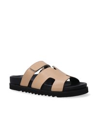 Beige leren slip-on sandaal met open teen, zwarte rubberen zool en twee banden met uitsnijdingen en klittenbandsluiting.