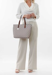 Šedá prošívaná taška přes rameno s hnědými koženými popruhy a kulatým kovovým ozdobným prvkem. Má obdélníkový tvar a pevnou základnu s viditelným prošitím.