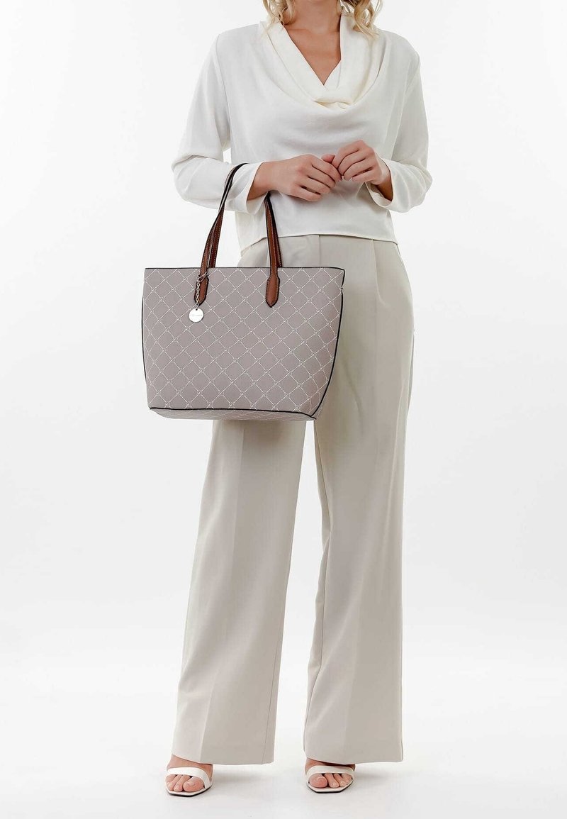 Šedá prošívaná taška přes rameno s hnědými koženými popruhy a kulatým kovovým ozdobným prvkem. Má obdélníkový tvar a pevnou základnu s viditelným prošitím.