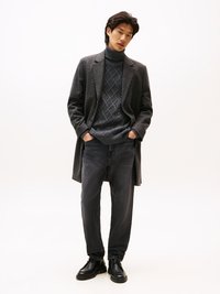 Manteau à carreaux gris sur un pull à col montant gris foncé avec des motifs en losange, associé à un jean ample foncé et des chaussures noires.