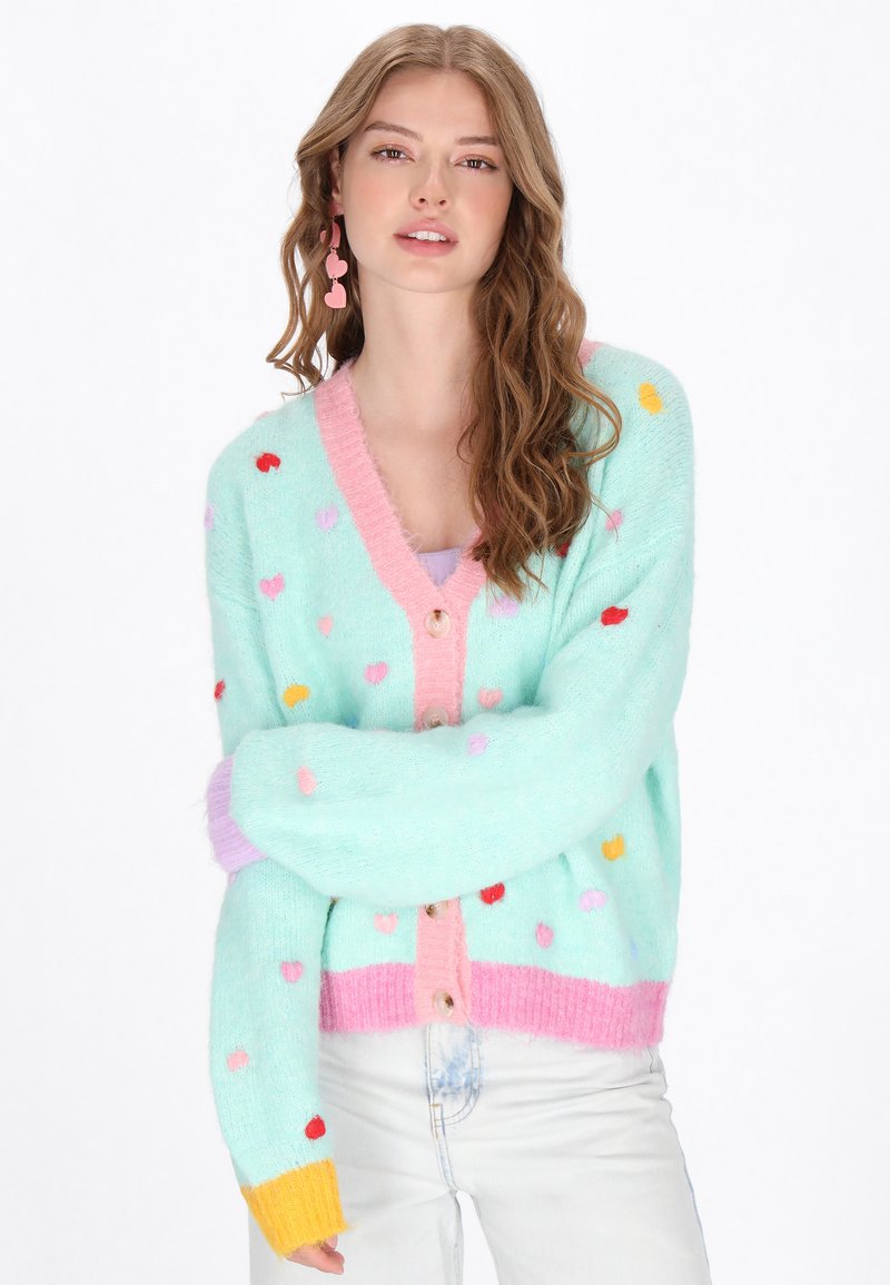Hellblau, fluffige Strickjacke mit mehrfarbigen Herzmustern, pinkem Saum und bunten Bündchen. Verfügt über runde Knöpfe an der Vorderseite.