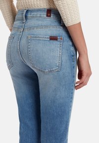 Jeans di denim azzurro chiaro con vita alta, dotati di due tasche posteriori e dettaglio in pelle marrone con marchio sulla cintura. Texture liscia.