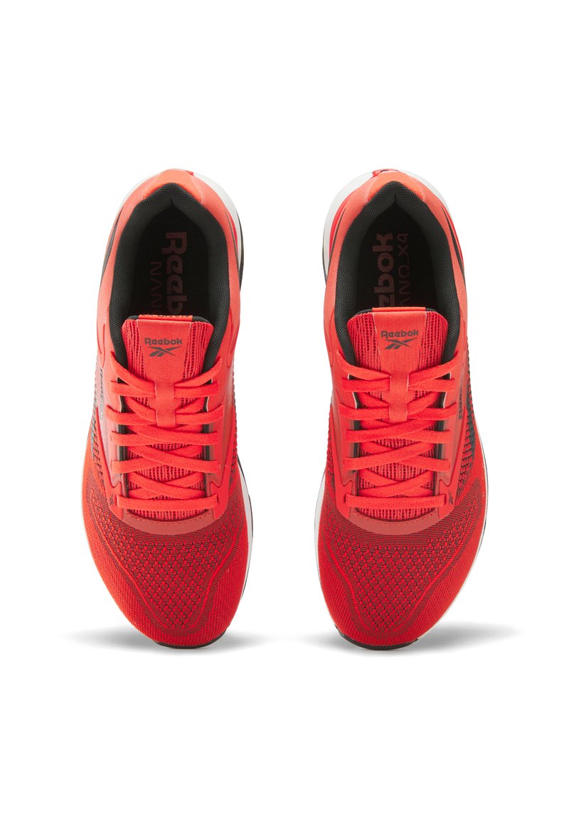 Zapatillas deportivas rojas con parte superior de malla, detalles texturizados, cordones planos y suela blanca. Presentan la marca Reebok en la lengüeta y el costado.