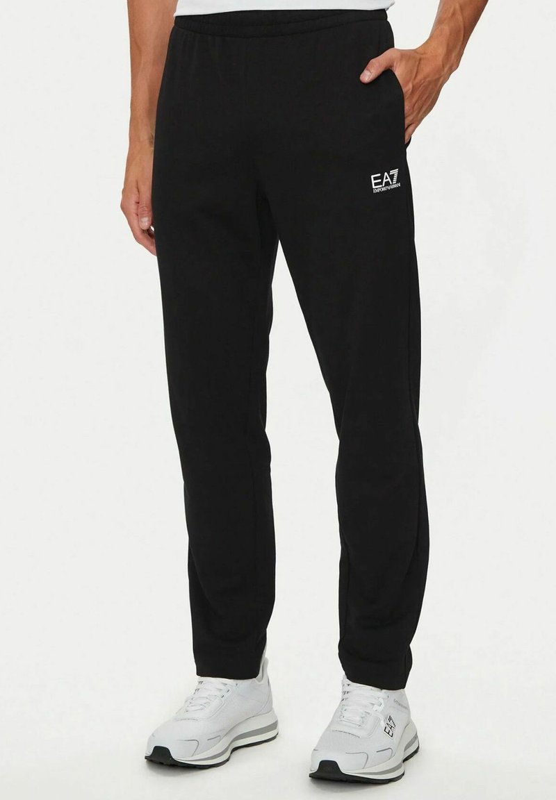 Pantaloni sportivi neri realizzati in tessuto morbido con cintura elastica. Presentano tasche laterali e un piccolo logo EA7 bianco sulla coscia sinistra.