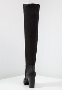 Zwarte boven-de-knie laars van suede met een glad leren hak. Heeft een taps toelopende vorm, een gestructureerd lichaam en een chunky hak voor stabiliteit.