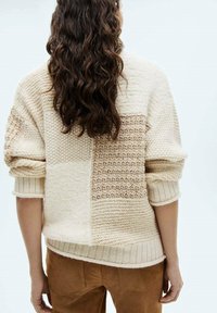 Cremfarbener Strickpullover mit einem strukturierten Patchwork-Design; verfügt über ribbelte Bündchen und Saum und zeigt unterschiedliche Strickmuster sowie ein weiches, gemütliches Material.