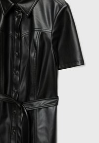 Robe noire à manches courtes en simili cuir avec des boutons sur le devant, col, coutures visibles et ceinture nouée à la taille.