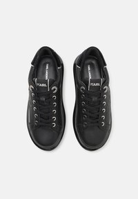 Black sneakers with a smooth leather exterior, round toe, and silver eyelets. Features a textured sole and logo on the tongue.