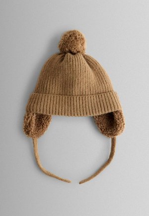 Brauner Strickhut mit geripptem Design, einem flauschigen Pompon oben und Ohrenklappen, die mit weichem, strukturiertem Stoff gefüttert sind. Mit Bändern für einen sicheren Sitz.