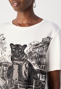 Witte katoenen T-shirt met een zwarte pailletten cartoon panter met een sjaal, voor een schets van stedelijke architectuur. Ronde halslijn, korte mouwen.