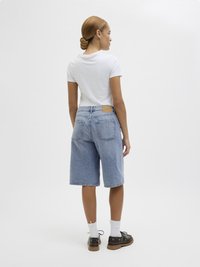 Shorts de ganga azul claro com um corte descontraído, com detalhes em remendo na parte de trás, combinados com uma t-shirt justa branca e sapatos castanhos.