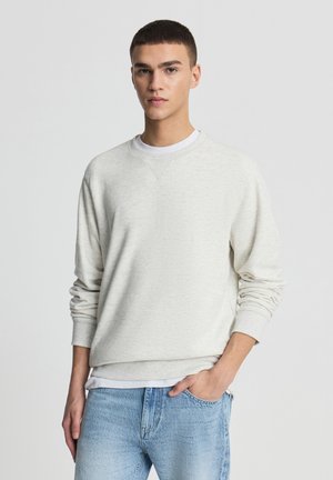 Felpa grigia chiaro realizzata in tessuto strutturato, con scollo a girocollo e polsini a costine, abbinata a jeans in denim blu.