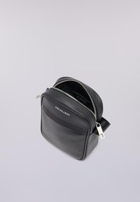 Zaino in pelle nera testurizzata con zip argentata, tasca frontale e etichetta del marchio. Forma rettangolare compatta con tracolla regolabile.