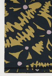 Tissu multicolore présentant des formes abstraites jaunes et roses sur un fond sombre, avec un ourlet noir cousu et une étiquette de logo.