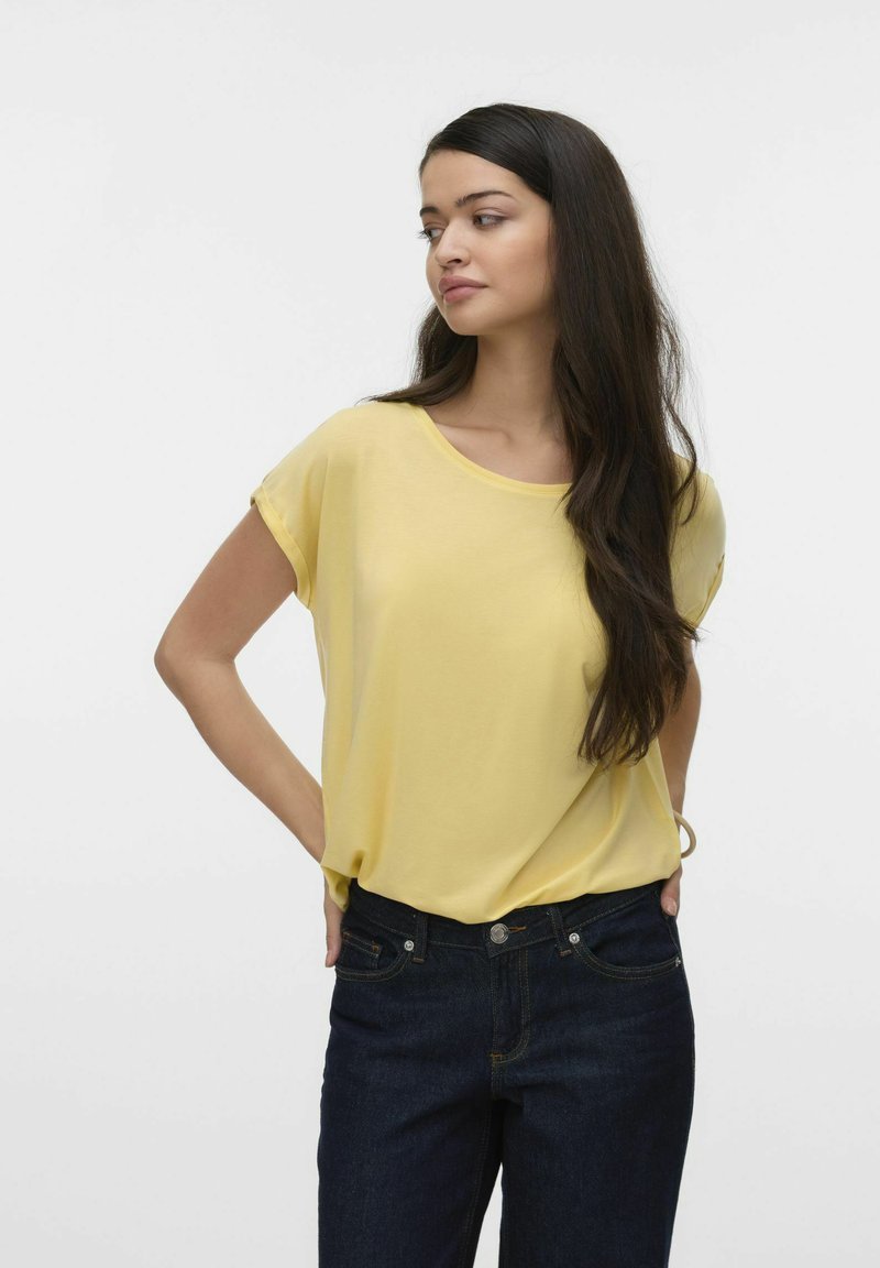 Short-sleeve yellow blouse in soft fabric with a round neckline, paired with dark denim jeans featuring side pockets and a button closure.