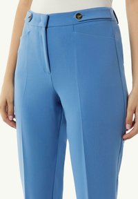Pantalons ajustés bleu clair avec une texture lisse, dotés de deux poches avant et de boutons dorés à la taille.