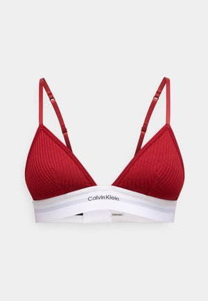 Rode geribbelde bralette met verstelbare bandjes en een witte elastische band met het "Calvin Klein" logo. Gladde textuur, driehoekige cups, minimalistisch ontwerp.