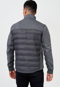 Graue Jacke mit Reißverschluss, mit einem strukturierten, gestrickten oberen Abschnitt und einem glatten, gesteppte unteren Abschnitt. Verfügt über einen hohen Kragen und elastische Bündchen.