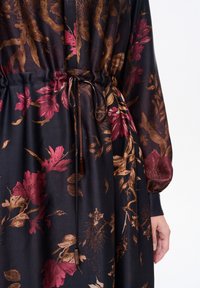 Sukienka w kwiatowy wzór na ciemnej tkaninie, z odcieniami bordo i złota, z marszczoną talią i wiązaniem, z długimi rękawami.