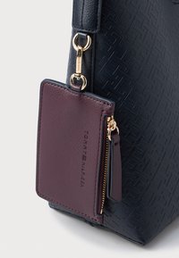 Granatowa torebka ze strukturalnej skóry z przymocowaną bordową kieszonką na zamek, złote akcenty metalowe oraz minimalistyczny geometryczny wzór.