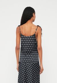 Zwart mouwloos topje met witte polka dots, gemaakt van een gladde stof. Heeft dunne bandjes en een losse pasvorm, met zijstrikdetails.