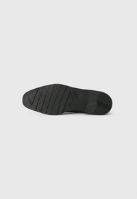 Suela de zapato de goma negra con ranuras horizontales y patrones de tracción diagonales. Presenta un ligero arco y un área del talón reforzada.