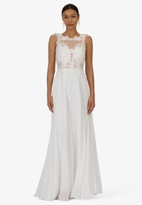 Robe blanche avec un bustier en dentelle florale transparente et un décolleté en forme de scallop, accompagnée d'une jupe fluide. De longues lignes élégantes créent une silhouette raffinée.