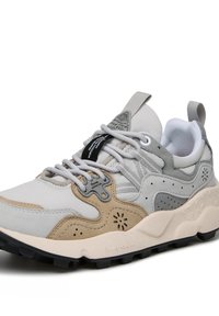 Lichtgrijze en beige sneaker met een gestructureerd ontwerp, voorzien van een zwart label, grijze veters en een robuuste zwarte zool voor grip.