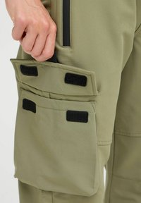 Cargo pants in olive green fabric, featuring prominently displayed black Velcro pockets and a smooth texture. Tailored fit with side accents.